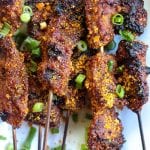 nigerian beef suya kebabs on white plate with green onions