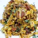 indian fried cabbage on a white plate with tomatoes and fresh herbs