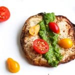 Roasted celery root steak on a plated topped with cherry tomatoes and collard greens salsa verde